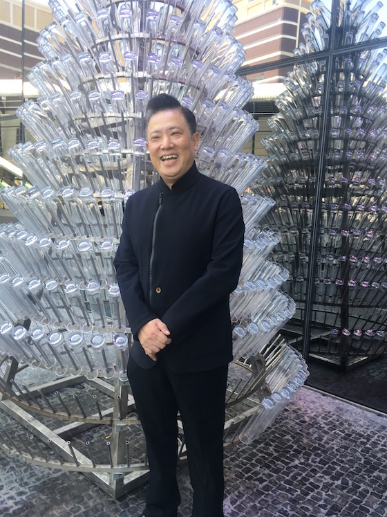 Paul Kwok in front of a metal frame being decorated with recycled bottles